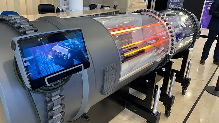  A metal cylinder lays on its side with metal bracings and a view screen. much of the visible cannister is clear, revealing lit red/orange rods. 