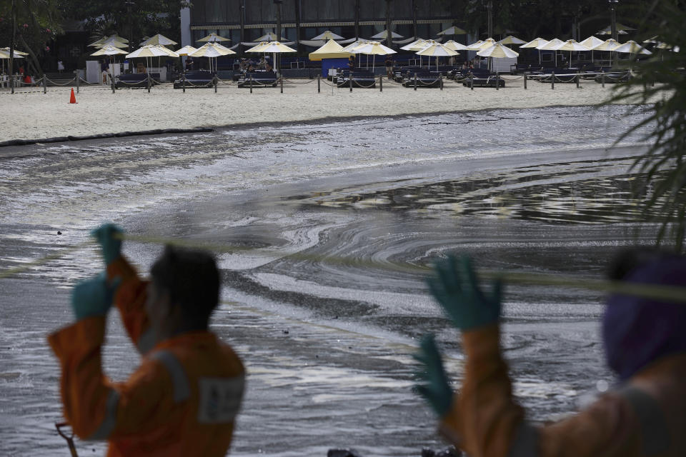 Workers prepare to clean oil spill as visitors hang out at Sentosa's Tanjong Beach area in Singapore, Sunday, June 16, 2024. An oil spill caused by a dredger boat hitting a stationary cargo tanker has blackened part of Singapore’s southern coastline, including the popular resort island of Sentosa, and sparked concerns it may threaten marine wildlife. (AP Photo/Suhaimi Abdullah)