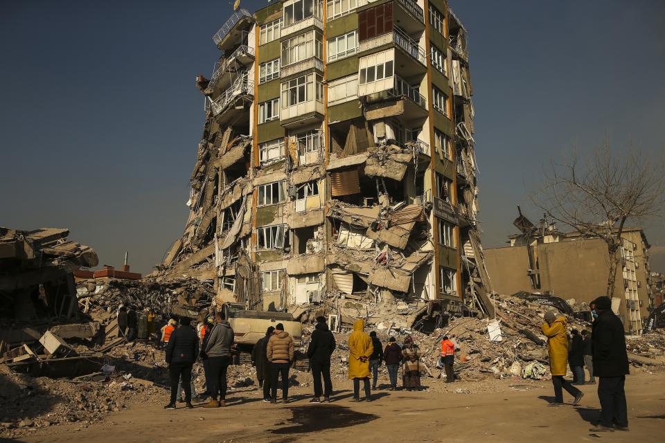 People stand by a collapsed building in Kahramanmaras, southern Turkey, Sunday, Feb. 12, 2023. Ever since the powerful 7.8 earthquake that has become Turkey's deadliest disaster in modern history, survivors have been gathering outside destroyed buildings, refusing to leave. (AP Photo/Emrah Gurel)