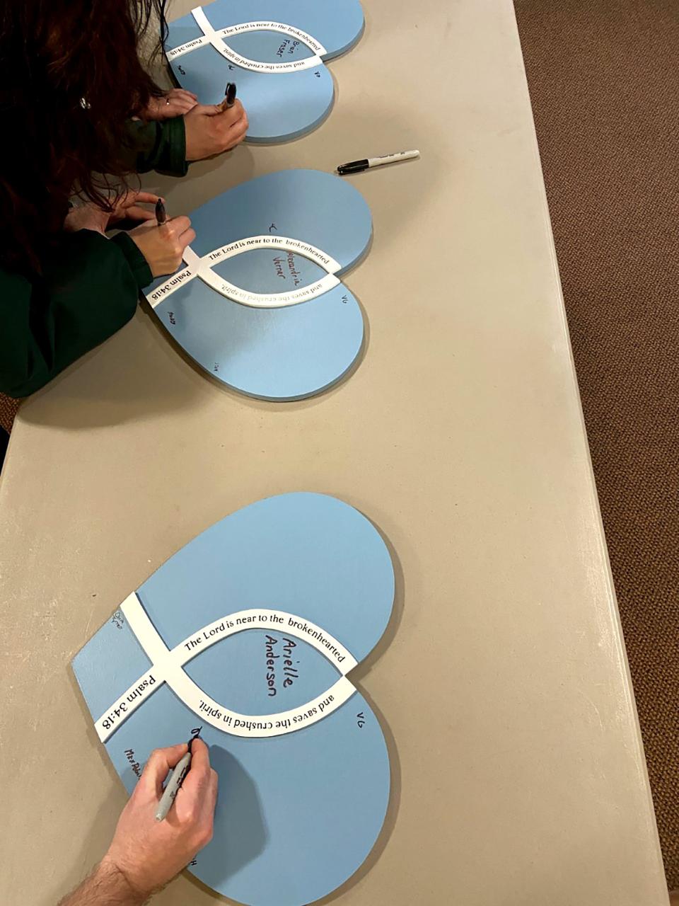 People use Sharpies to sign their names on three blue and white wooden hearts with the names of the three MSU shooting victims who died Monday in the center, following a prayer service at Martin Luther Chapel in East Lansing on Tuesday, Feb. 14, 2023. The hearts will soon be displayed on white crosses. 