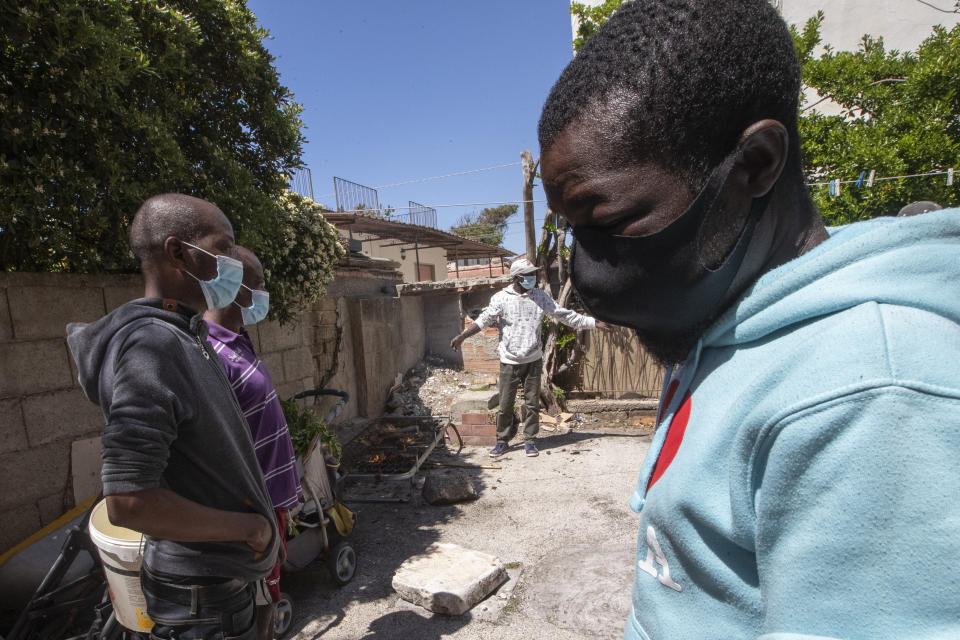 In this photo taken on Monday, April 27, 2020, a man uses an old bed frame as a stove as he cooks some chickens on the mattress springs surrounded by his home-mates, all migrants from Nigeria and Ghana, in Castel Volturno, near Naples, Southern Italy. They are known as “the invisibles,” the undocumented African migrants who, even before the coronavirus outbreak plunged Italy into crisis, barely scraped by as day laborers, prostitutes and seasonal farm hands. Locked down for two months in their overcrowded apartments, their hand-to-mouth existence has grown even more precarious with no work, no food and no hope. (AP Photo/Alessandra Tarantino)