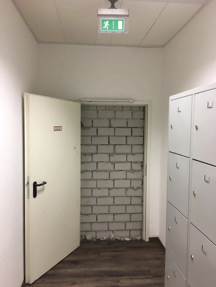 An emergency exit door opens to reveal a brick wall with no passage through it