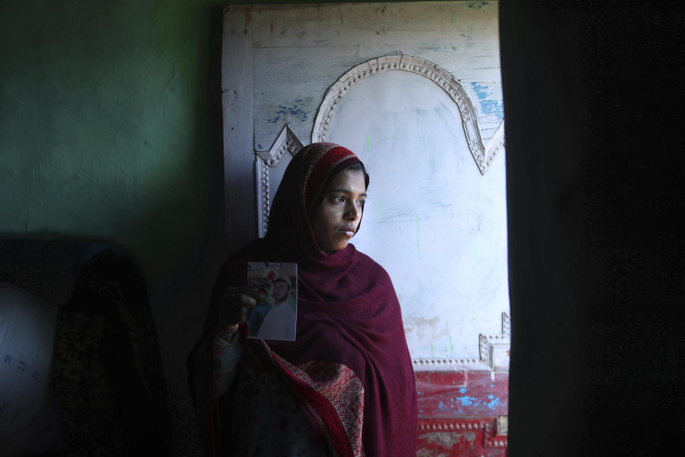 Safina Bi, who alleges her husband Altaf Hussain was killed by Pakistan army while ferrying ration supplies to one of the Indian army border posts, stands holding a picture of her husband at her house in Poonch, India, Wednesday, Dec. 16, 2020. The terrain is tough and the life of civilians living in the area is even tougher, with them often caught in the line of fire along the Line of Control, that for the past 73 years divided the region between the two nuclear-armed rivals of India and Pakistan. Over the last year, troops from the two sides have traded fire almost daily along the frontier, leaving dozens of civilians and soldiers dead. (AP Photo/Channi Anand)