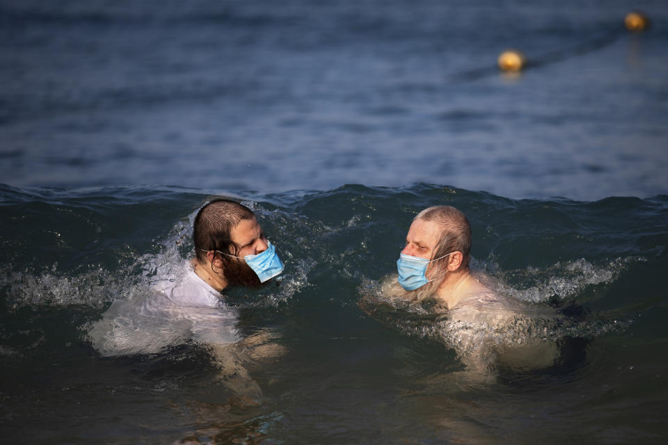 Ultra-orthodox Jewish men wearing protective face masks swim in the Mediterranean Sea, on a beach segregated for males three days a week, in Tel Aviv, Israel, Wednesday, July 8, 2020. In an effort to quell the rapid spread of the coronavirus, Israel has re-imposed a series of restrictions on the public. This week, the Israeli government limited gatherings and ordered reception halls, restaurants, bars, theaters, fitness centers and pools be shut down again. (AP Photo/Oded Balilty)
