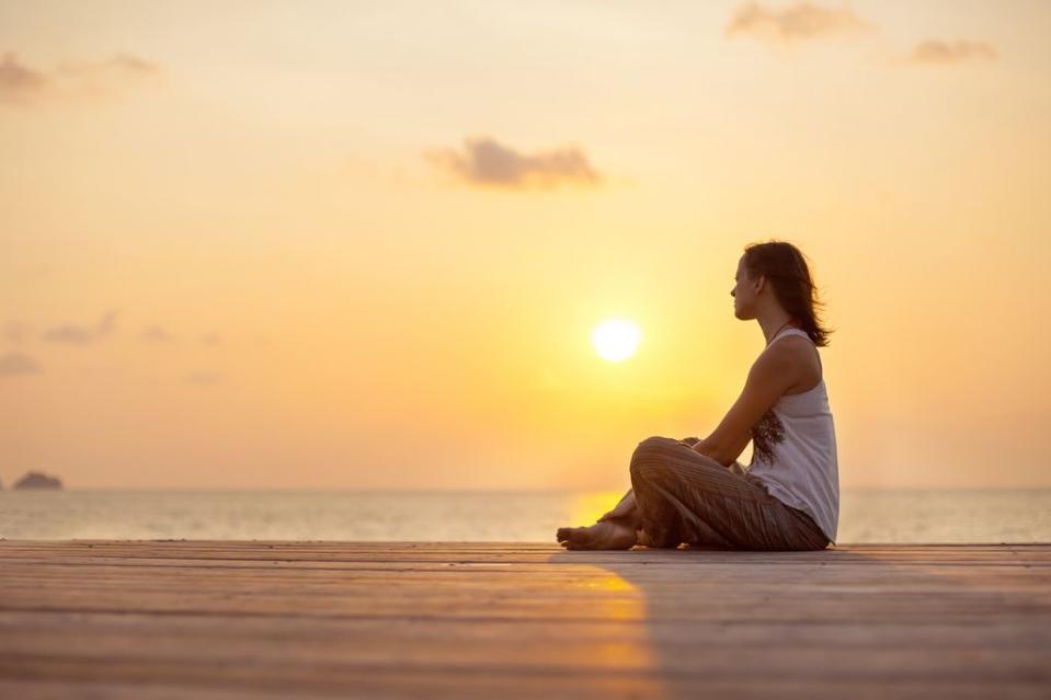 mujer relajada en el muelle junto al mar en la puesta de sol