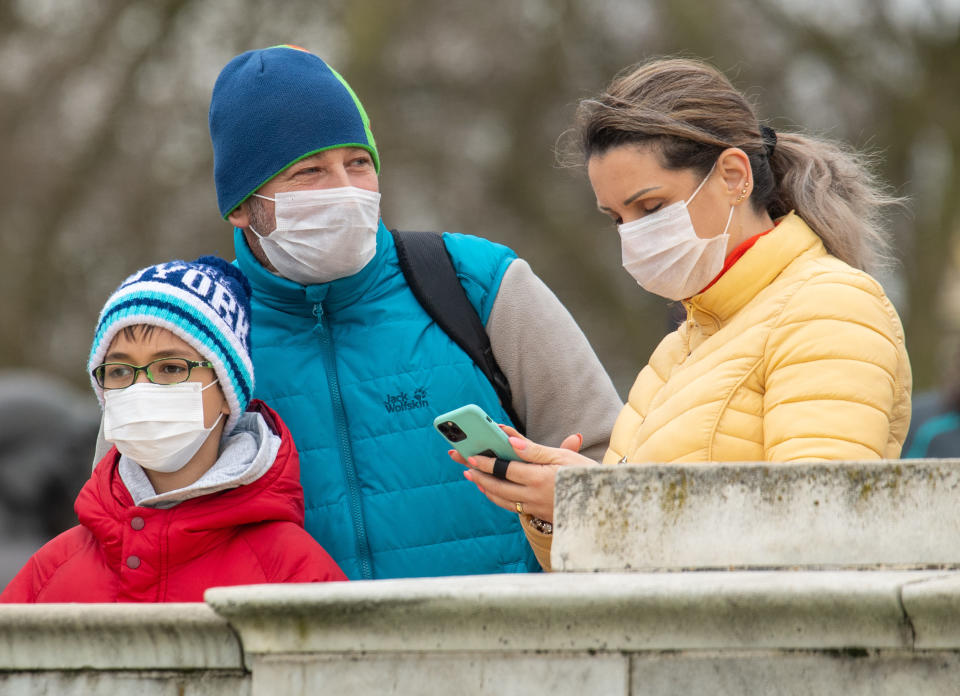 People wearing protective face masks watch the Changing of the Guard ceremony outside Buckingham Palace, London, the day after the Prime Minister said that Covid-19 "is the worst public health crisis for a generation", and the government's top scientist warned that up to 10,000 people in the UK are already infected. PA Photo. Picture date: Friday March 13, 2020. See PA story HEALTH Coronavirus. Photo credit should read: Dominic Lipinski/PA Wire (Photo by Dominic Lipinski/PA Images via Getty Images)