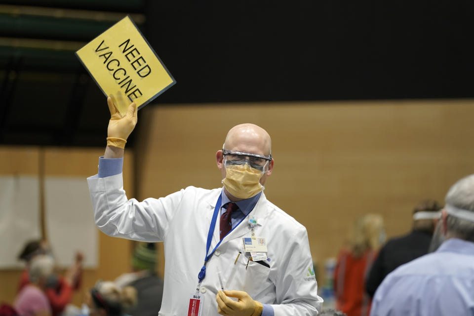 Dr. John Corman, the chief clinical officer for Virginia Mason Franciscan Health, holds a sign that reads "Need Vaccine" to signal workers to bring him more doses of the Pfizer vaccine for COVID-19, Sunday, Jan. 24, 2021, as he works at a one-day vaccination clinic set up in an Amazon.com facility in Seattle. (AP Photo/Ted S. Warren)