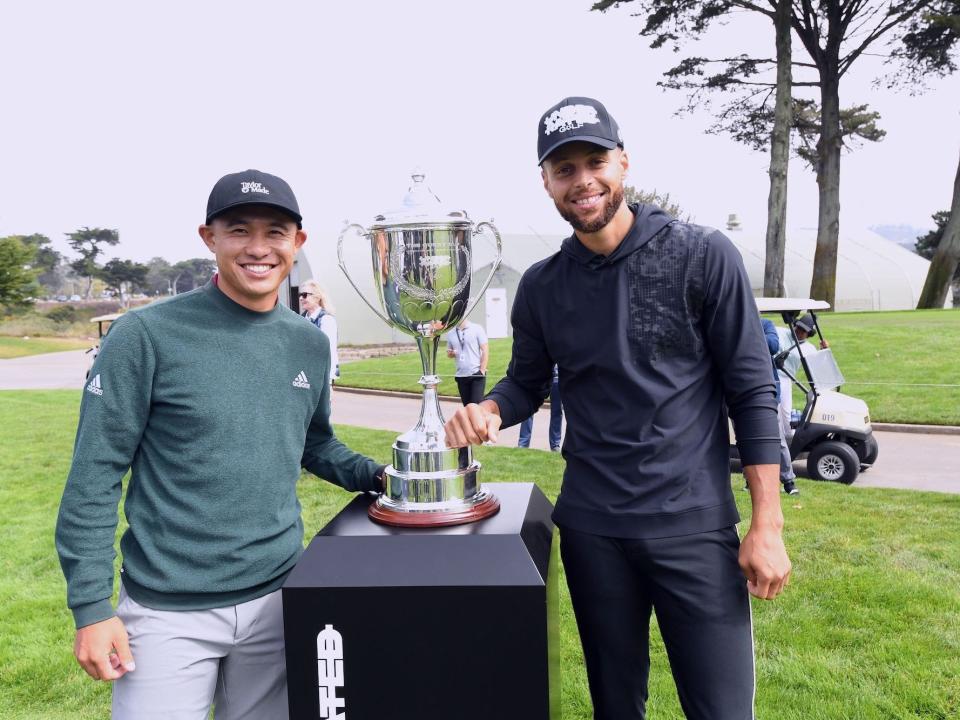 Collin Morikawa poses with a trophy next to Stephen Curry at a golf event.