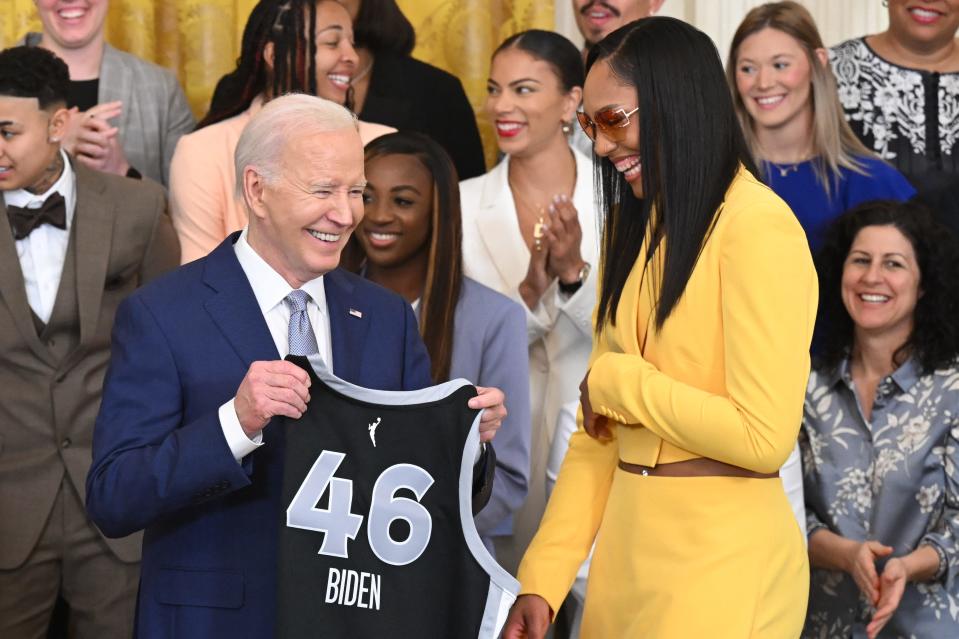 President Joe Biden, with Las Vegas Aces player A'ja Wilson, holds up a jersey given to him by the team during an event to recognize the 2023 WNBA champions in the East Room of the White House in Washington, D.C., on May 9, 2024. Former Iowa State star Ashley Joens is shown top right, wearing a blue dress.