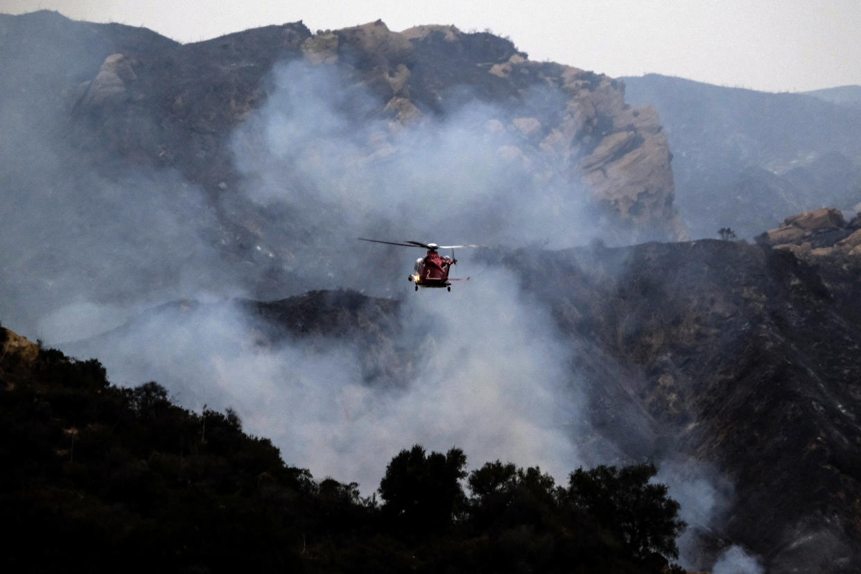 A firefighting helicopter prepares to drop water onto a wildfire in the Pacific Palisades area of Los Angeles, Sunday, May 16, 2021. (AP Photo/Ringo H.W. Chiu)