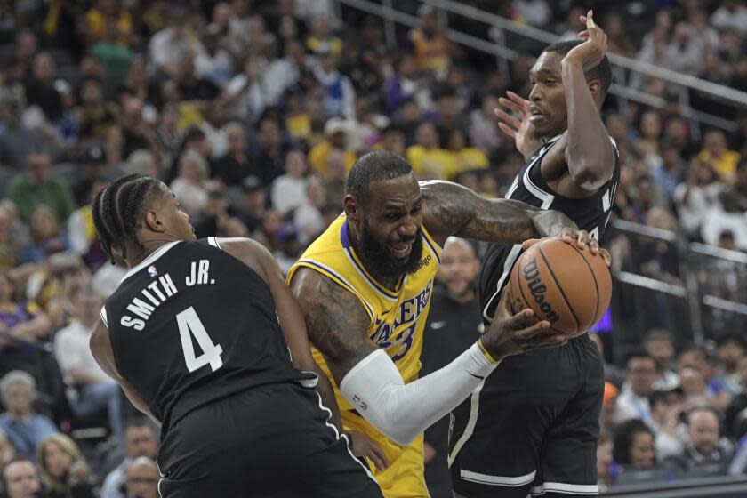 Los Angeles Lakers forward LeBron James (center) takes a shot at Brooklyn Nets guard Dennis Smith Jr. (4) during the first half of an NBA preseason game in Las Vegas on Monday, Oct. 9, 2023. ) and Lonnie Walker IV (right).  (AP Photo/Sam Morris)