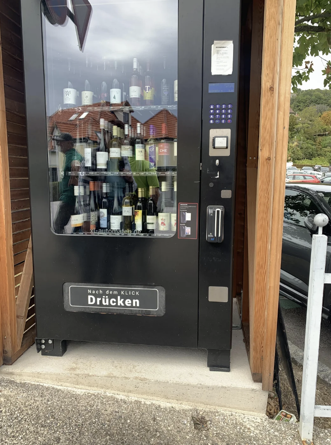 Wine vending machine outside with a selection of bottles, "Nach dem Klick Drücken" written on the bottom