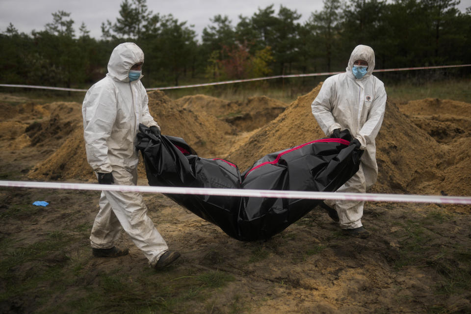 Members of a forensic team carry a plastic bag with a body inside as they work at an exhumation in a mass grave in Lyman, Ukraine, Tuesday, Oct. 11, 2022. (AP Photo/Francisco Seco)