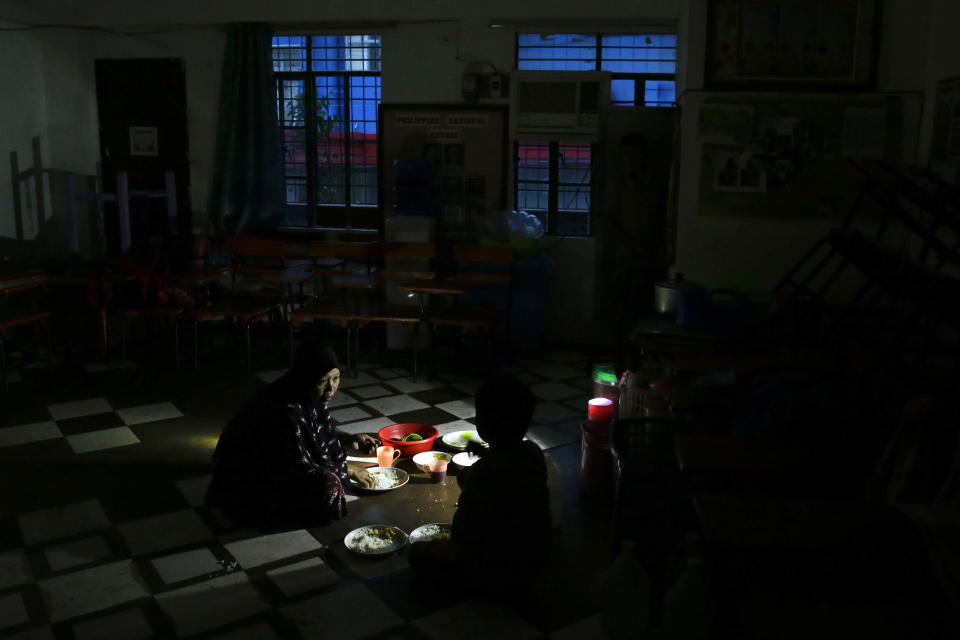 A woman and her son eats a meal using a flashlight inside a temporary evacuation center as electricity was shut-off following the onslaught of Typhoon Mangkhut in Tuguegarao city in Cagayan province, northeastern Philippines, Saturday, Sept. 15, 2018. The typhoon slammed into the Philippines northeastern coast early Saturday, it's ferocious winds and blinding rain ripping off tin roof sheets and knocking out power, and plowed through the agricultural region at the start of the onslaught. (AP Photo/Aaron Favila)