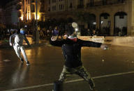 Anti-government protesters throw stones against the riot police, during ongoing protests against the political elites who have ruled the country since decades, in Beirut, Lebanon, Sunday, Jan. 19, 2020. (AP Photo/Hassan Ammar)