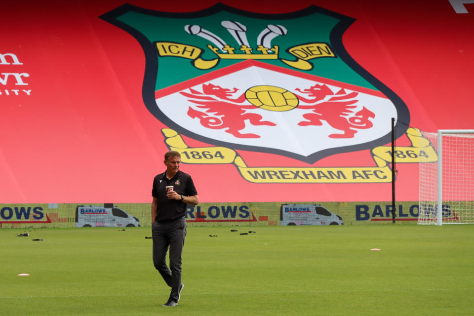 In this photo provided by Wrexham FC, Wrexham manager Phil Parkinson is seen in front of the new Kop banner the Racecourse Ground in Wrexham, Wales, Saturday, Sept. 18, 2021. It has been described as a “crash course in football club ownership” and the two Hollywood stars who bought a beleaguered team in English soccer's fifth tier with the lofty aim of transforming it into a global force are certainly learning on the job.(Gemma Thomas/Wrexham FC via AP)