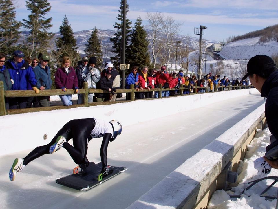 A person gets ready for a skeleton run with a crowds and trees behind them