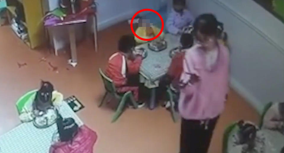 A child's head, which is circled in this photo, is seen falling backwards as a teacher films other students on her mobile phone.