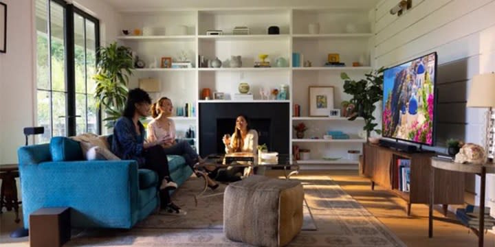 A living room with two people watching TV with the Vizio V-Series 2.1 Home Theater Soundbar and subwoofer underneath.