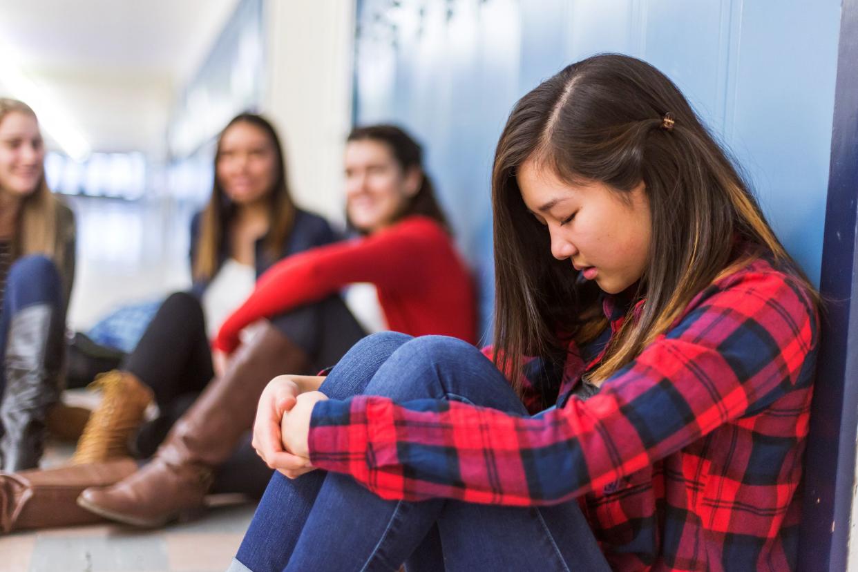 Girl sitting against her locker being bullied by girls in background