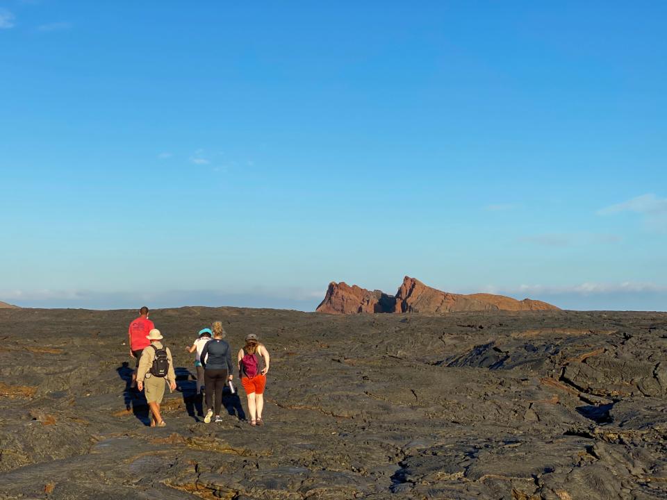 Group of people walking on hardened lava in front of blue skies