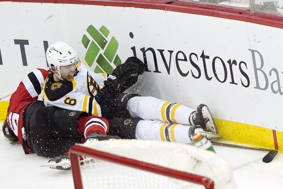Boston Bruins defenseman Mike Reilly (6) and New Jersey Devils center Jack Hughes (86) collide against the boards behind the Bruins net during the second period of an NHL hockey game, Tuesday, May 4, 2021, in Newark, N.J. Hughes left the game after the collision. (AP Photo/Kathy Willens)