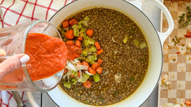 pouring tomato puree into pot of lentil vegetable soup