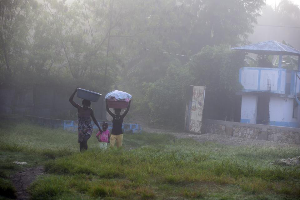 Malaika Pierre, 5, walks between her mother Rose Andre Leon, left, and cousin Geraldine Pierre on the former UN base as they make their way to the Meille River to wash clothes in Mirebalais, Haiti, at sunrise Monday, Oct. 19, 2020. Ten years after a cholera epidemic swept through Haiti and killed thousands, families of victims still struggle financially and await compensation from the United Nations as many continue to drink from and bathe in a river that became ground zero for the waterborne disease. (AP Photo/Dieu Nalio Chery)