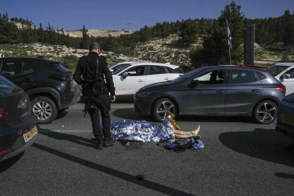 An Israeli police officer stands next to the body of a Palestinian attacker at the scene of a shooting attack near the West Bank settlement of Maale Adumim, Thursday, Feb. 22, 2024. Israel police said three Palestinian gunmen opened fire on the road near the settlement, killing one and wounding at least eight. Security forces on the site killed two of the gunmen, and a third was found during searches of the area afterwards and was detained. (AP Photo/Mahmoud Illean)