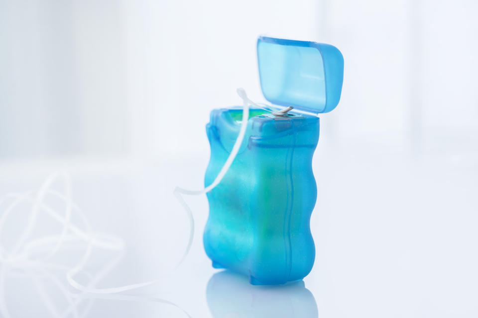 Dental floss container with string pulled out on a reflective surface