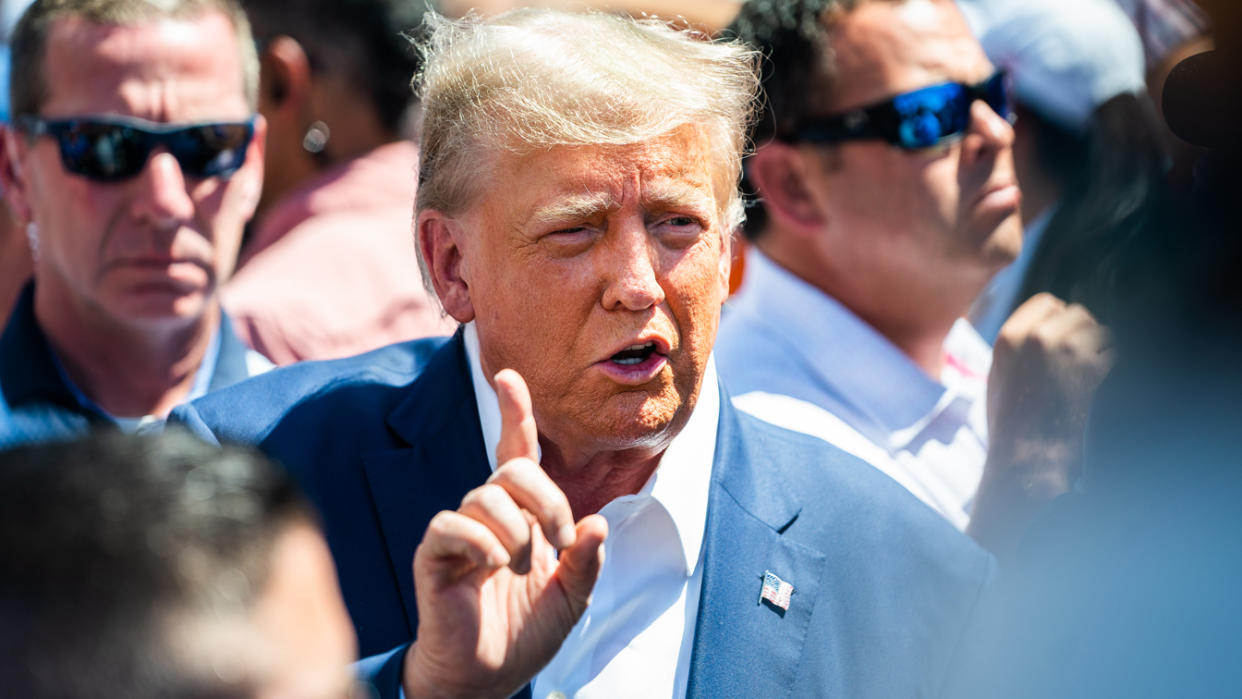 A blue-suited former President Donald Trump, without a signature tie, speaks with the press at the Iowa Pork Producers booth during the 2023 Iowa State Fair.