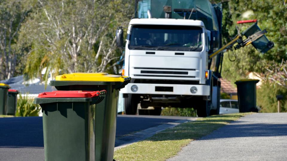 Focus on two Rubbish bins with rubbish truck in background lifting a bin.