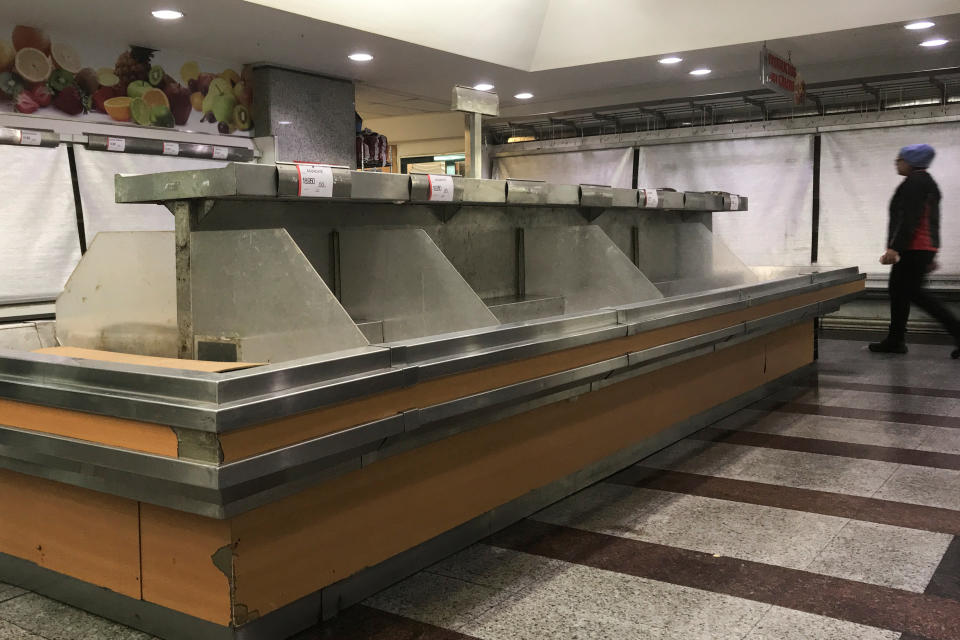 A woman walks past empty shelves at a store's fruit and vegetables section.