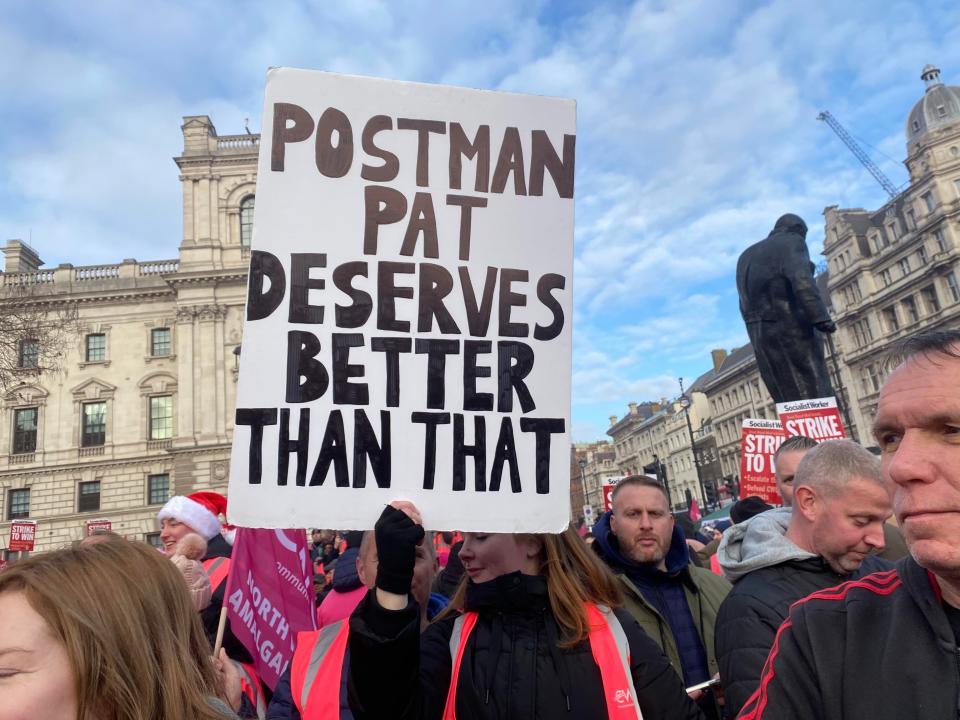 Striking postal worker holds placard reading ‘Postman Pat deserves better than that’ at Parliament Square rally (Mustafa Qadri/The Independent)