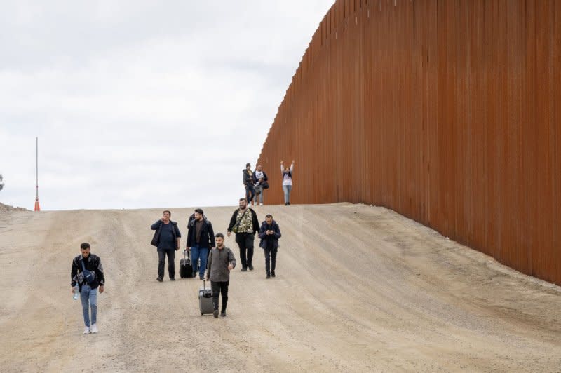 Migrants walk along the U.S. side of the border wall with Mexico to surrender to the U.S. Border Patrol near Campo, Calif., on March 13. File Photo by Pat Benic/UPI