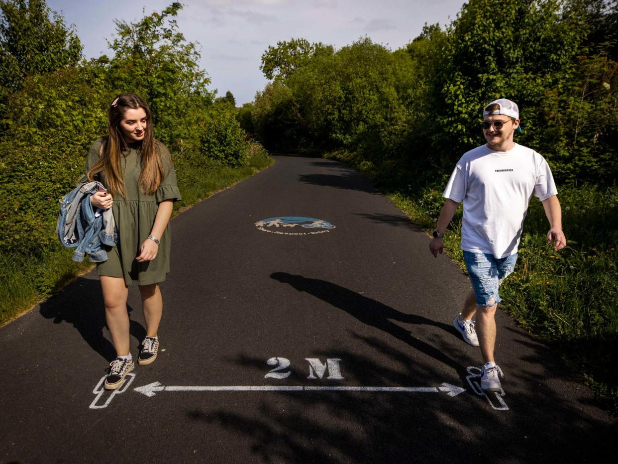 Gemma Gresslees with her friend Jason Close walking over the 2 metre social distancing sign on the Comber Greenway off Abbey Road in east Belfast, during the coronavirus lockdown, 26 May 2020: PA