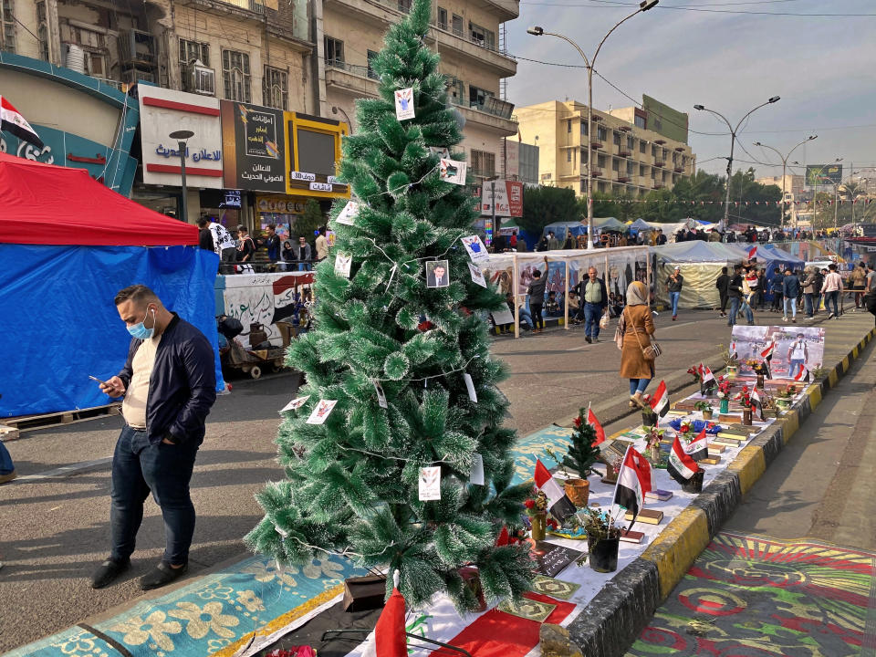 People pass by a Christmas tree with portraits of anti-government protesters who killed under fire from security forces in Tahrir Square during ongoing protests in Baghdad, Iraq, Thursday, Dec. 12, 2019. (AP Photo/Khalid Mohammed)