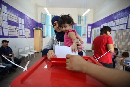 A woman carries a child as she casts her vote at a polling station during presidential election in Tunis