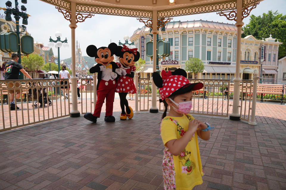 A girl wearing a face mask poses for a photograph with the iconic characters Mickey and Minnie Mouse at the Hong Kong Disneyland, Thursday, April 21, 2022. Hong Kong Disneyland reopened to the public after shutting down due to a surge in COVID-19 infections. (AP Photo/Kin Cheung)