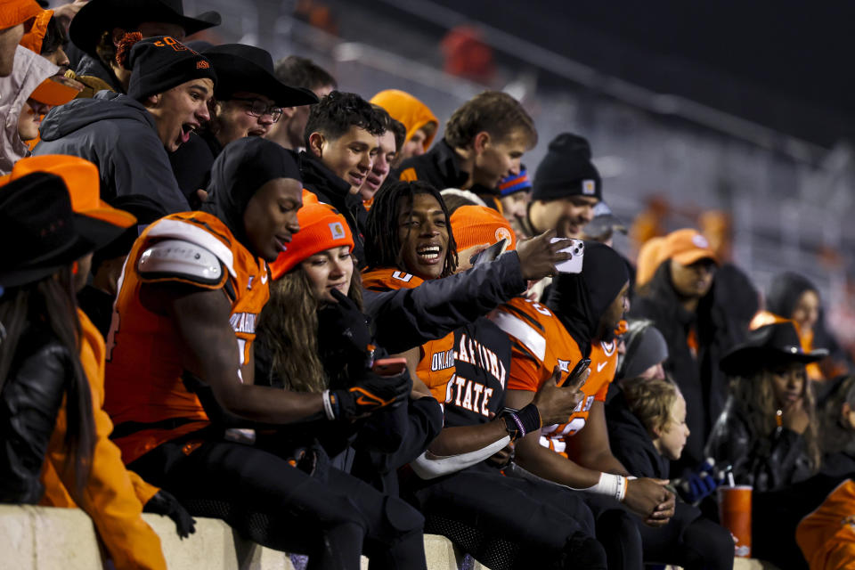 Oklahoma State running back Elijah Collins, left, running back Ollie Gordon II, center, and wide receiver Brennan Presley, right, celebrate with fans after the team's NCAA college football game against Cincinnati on Saturday, Oct. 28, 2023, in Stillwater, Okla. (AP Photo/Mitch Alcala)