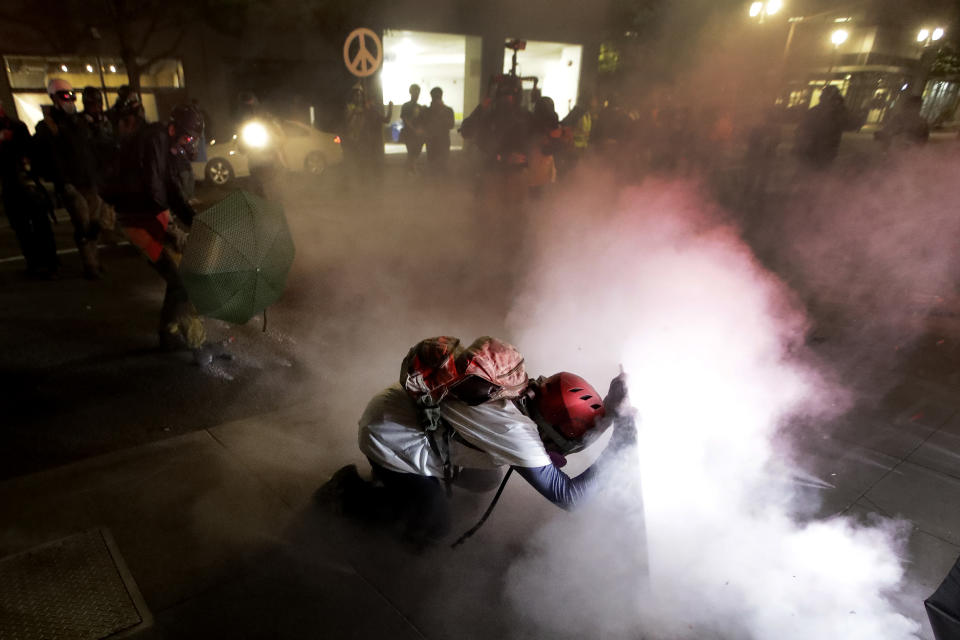 A demonstrator kneels and uses a makeshift shield as federal agents launch tear gas during a Black Lives Matter protest at the Mark O. Hatfield United States Courthouse Wednesday, July 29, 2020, in Portland, Ore. (AP Photo/Marcio Jose Sanchez)