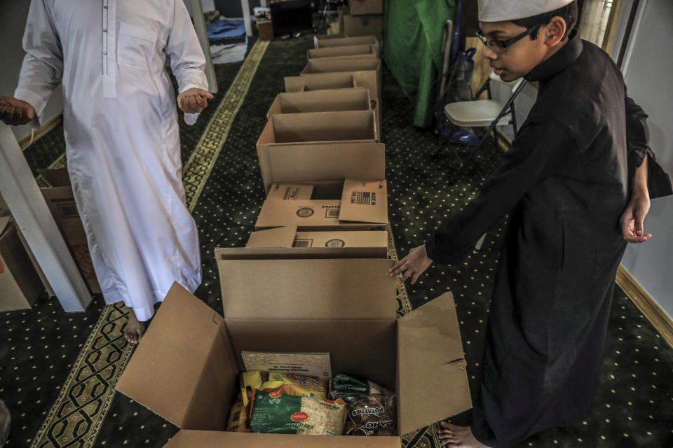 In this Wednesday, April 22, 2020, photo, Imam Mufti Mohammed Ismail, leader of An-Noor Cultural Center and masjid that serves a mostly Bangladeshi Muslim community in the Elmhurst neighborhood in the Queens borough of New York, and his son Hassan, 13, right, itemize boxes of food for distribution to those impacted by COVID-19 restrictions. Ismaill says this gives the center the opportunity to fulfill one of Ramadan's tenets — to serve those less fortunate, regardless of religion.. (AP Photo/Bebeto Matthews)