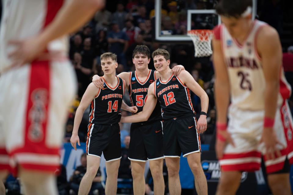 Princeton guard Matt Allocco (14) forward Zach Martini (54) and forward Caden Pierce (12) and teammates embrace in the final seconds of the Tigers' NCAA Tournament win over Arizona