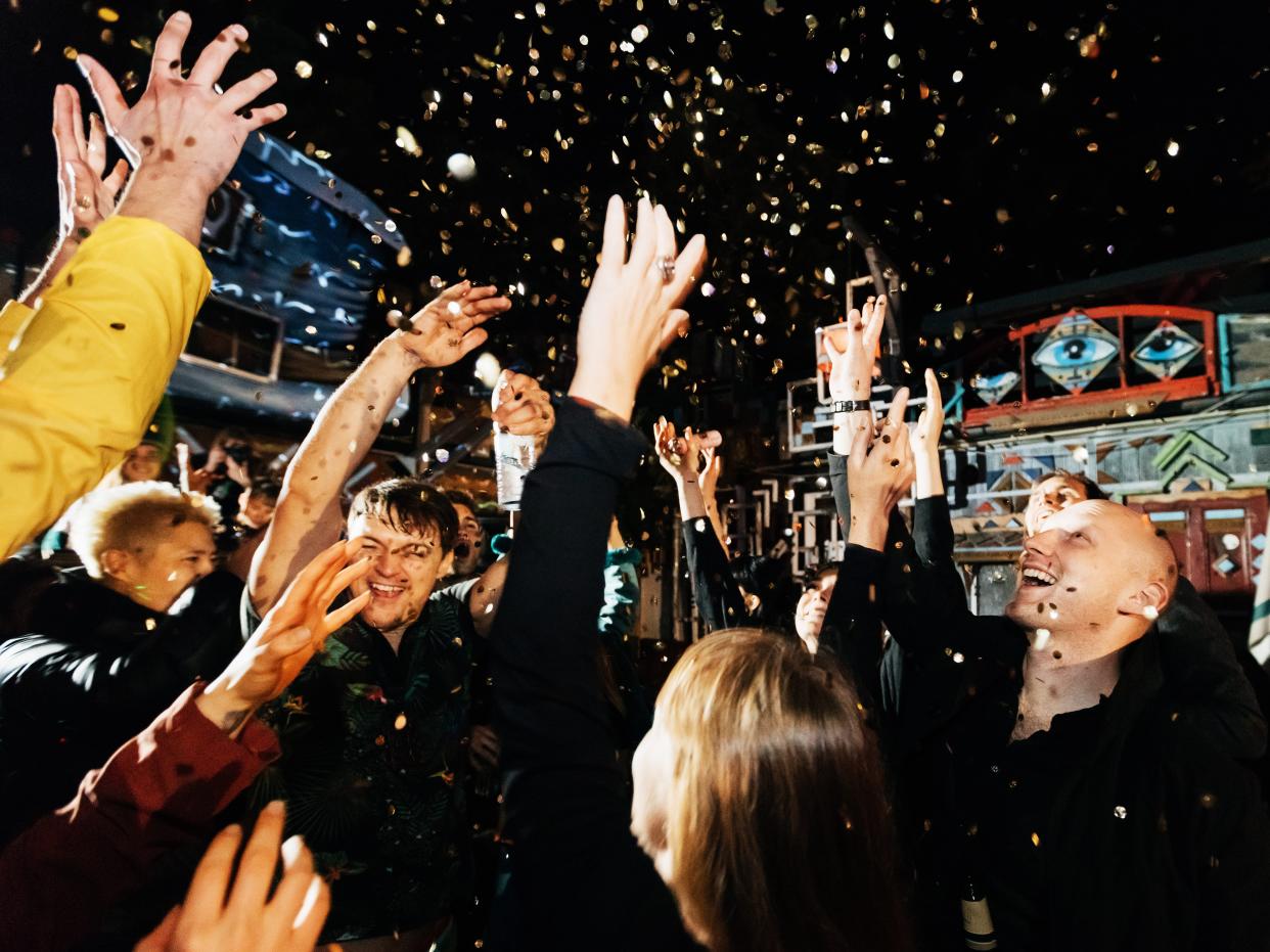 A group of friends celebrating throwing confetti in the air on the dance floor, having fun at an open air nightclub.