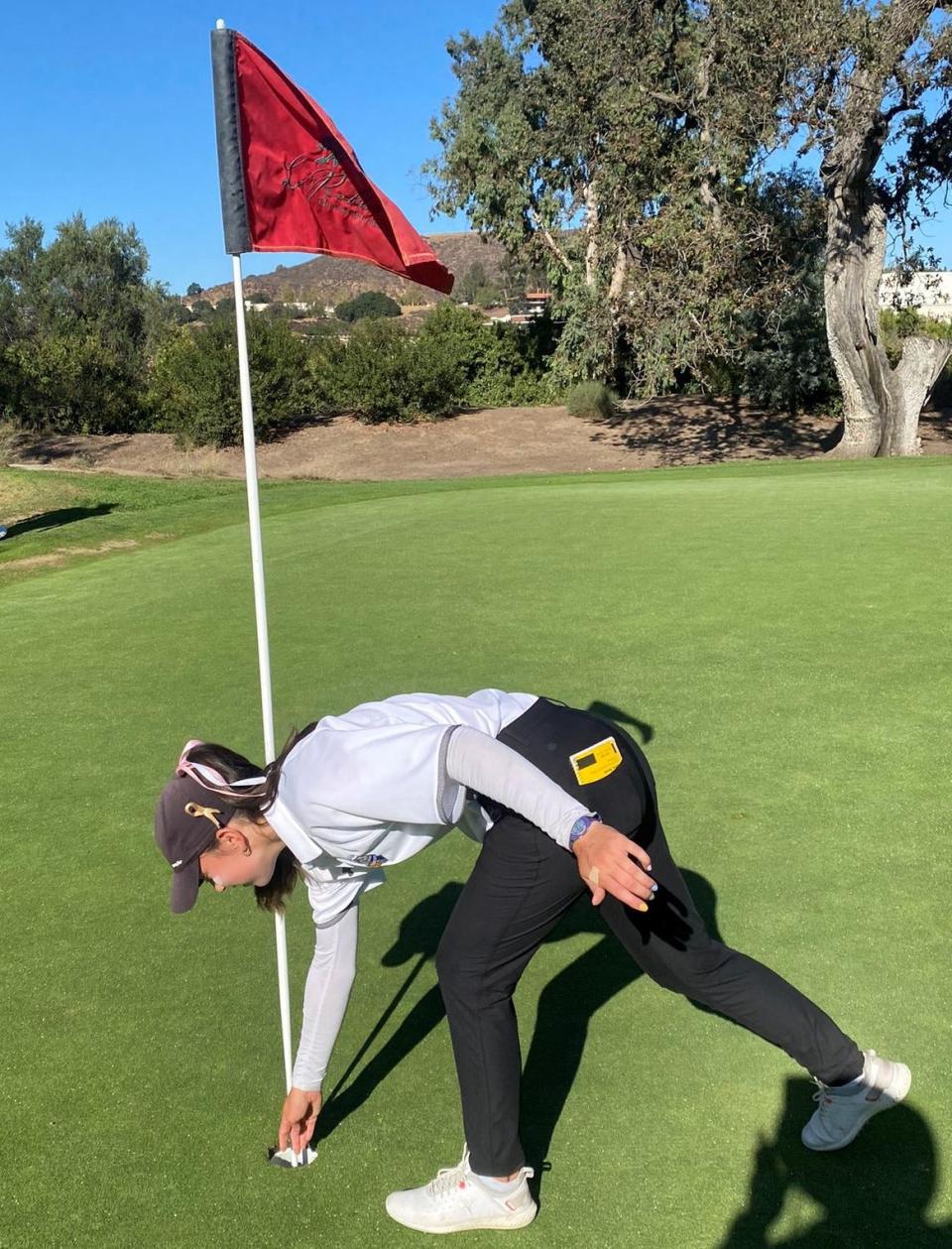 Agoura High's Lillian Spratt reaches into the cup to retrieve the ball after recording a hole in one during the Chargers' 209-221 win over Westlake at Los Robles Greens Golf Course on Tuesday.