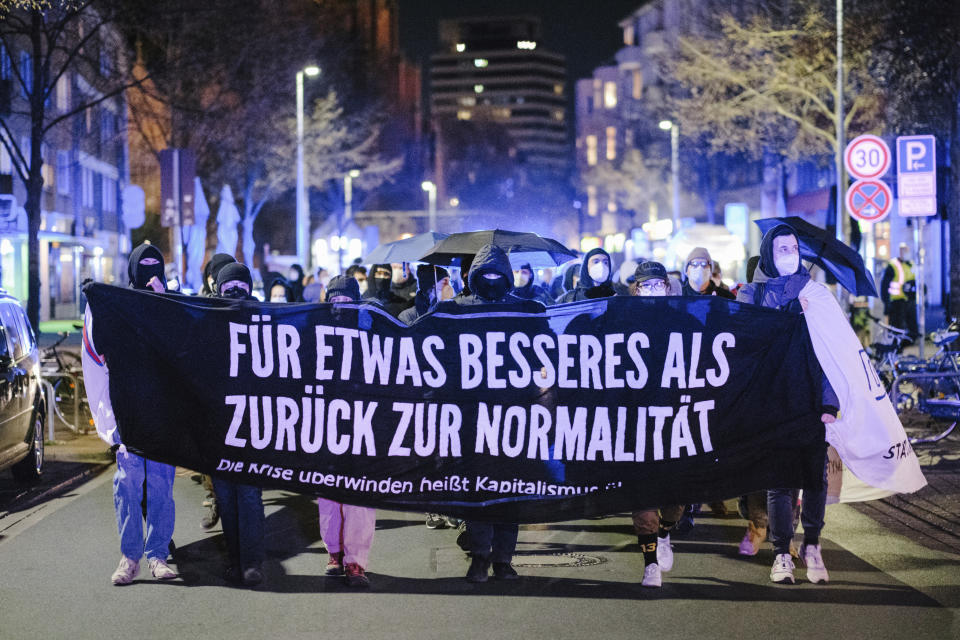 Participants in a demonstration against curfew restrictions walk through Nordstadt with a banner reading "For something better than back to normal" during the nightly curfew, in Hanover, Germany, Saturday, April 24, 2021. Federal coronavirus emergency curfew regulations have been in effect as of Saturday. This includes, among other things, curfew restrictions between 10 p.m. and 5 a.m. (Ole Spata/dpa via AP)