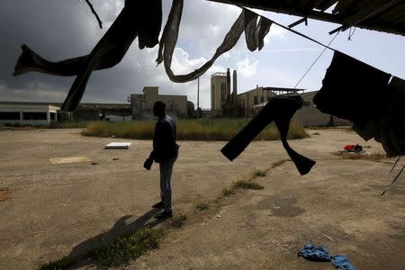 A Sudanese immigrant stands next to clothes that are hanging out to dry inside a deserted textile factory in the western Greek town of Patras April 28, 2015. REUTERS/Yannis Behrakis