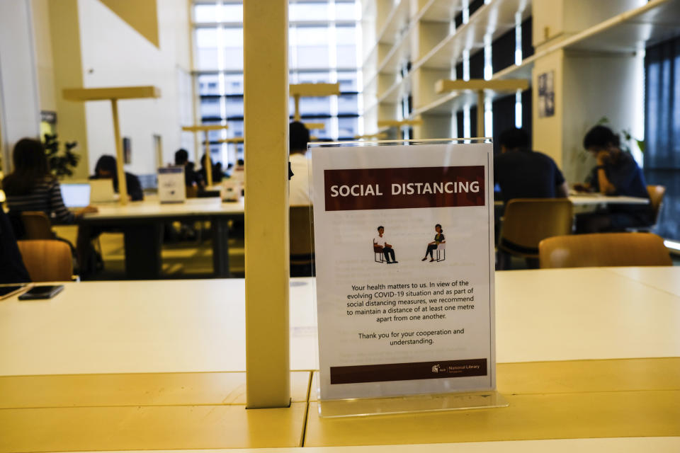 In this March 16, 2020, photo, a sign about social distancing is placed on a table at the National Library in Singapore. As the virus outbreak spreads ever further, it's becoming clear that some strategies are more likely to succeed in containing it: pro-active efforts to track down and isolate cases, access to basic, affordable public health and clear, reassuring messaging from leaders. (AP Photo/Ee Ming Toh)