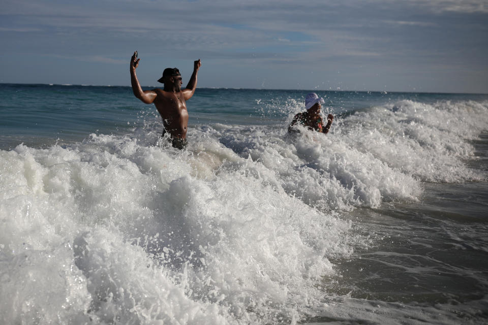 U.S. tourist Latron Evans and his partner Nika, frolicking ocean waters at the beach in Tulum, Quintana Roo state, Mexico, Monday, Jan. 4, 2021. Evans, a Mississippi firefighter, said he was impressed by the health measures due to the new coronavirus pandemic. "They're taking temperatures when you enter the building and giving you hand sanitizer every place you go, it's required. It's not that way in the states," he said. (AP Photo/Emilio Espejel)