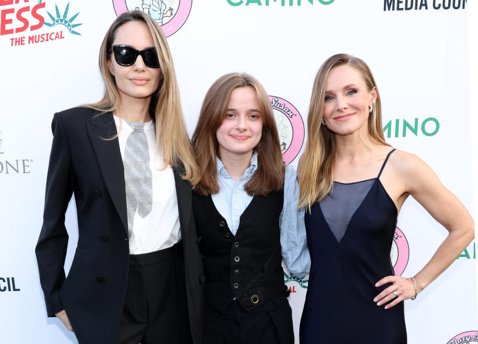 Angelina Jolie, Knox Jolie-Pitt, and Kristen Bell at a red carpet event; Angelina in a suit, Knox in a vest, and Kristen in a sleek dress